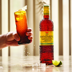 Hand, die einen Drink greift und ausschüttet, daneben die Flasche Mandarin Napoleon.