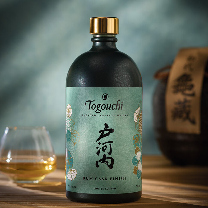Eine geschlossene Flasche Togouchi Rum Cask Finish neben einem gefüllten Whiskyglas auf einem Holztisch
